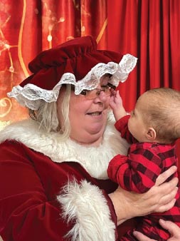 Woman dressed as Mrs. Claus playing with a baby